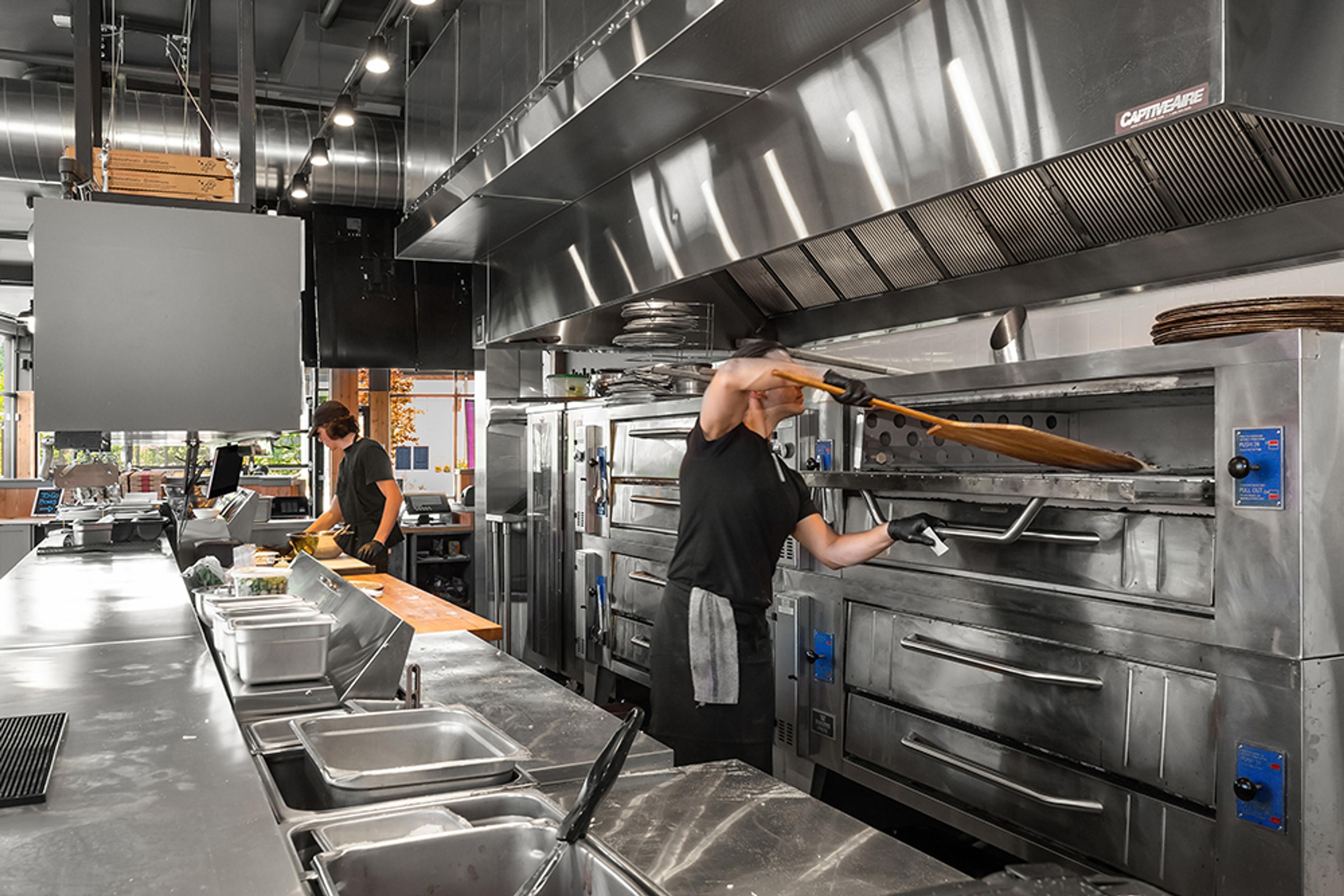 kitchen view with chef sliding pizza into deck oven