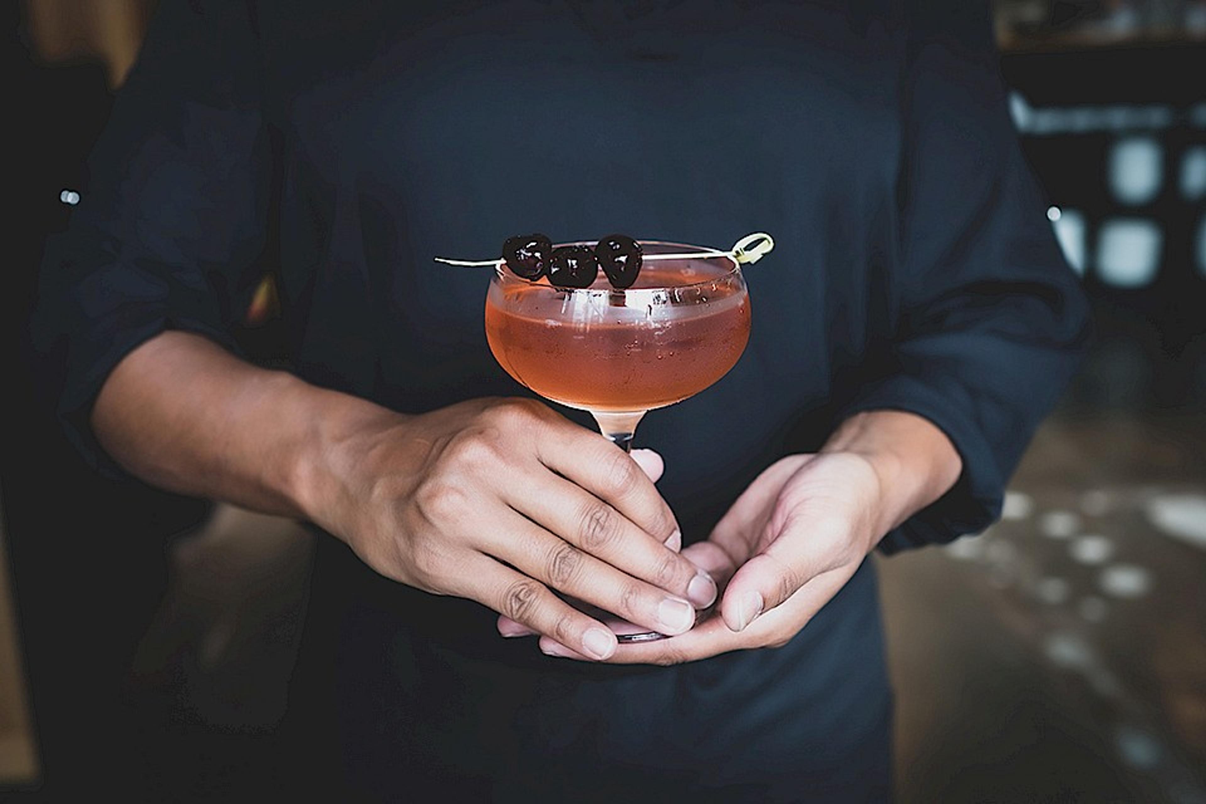 Server holding cocktail with brandied cherries in coupe glass