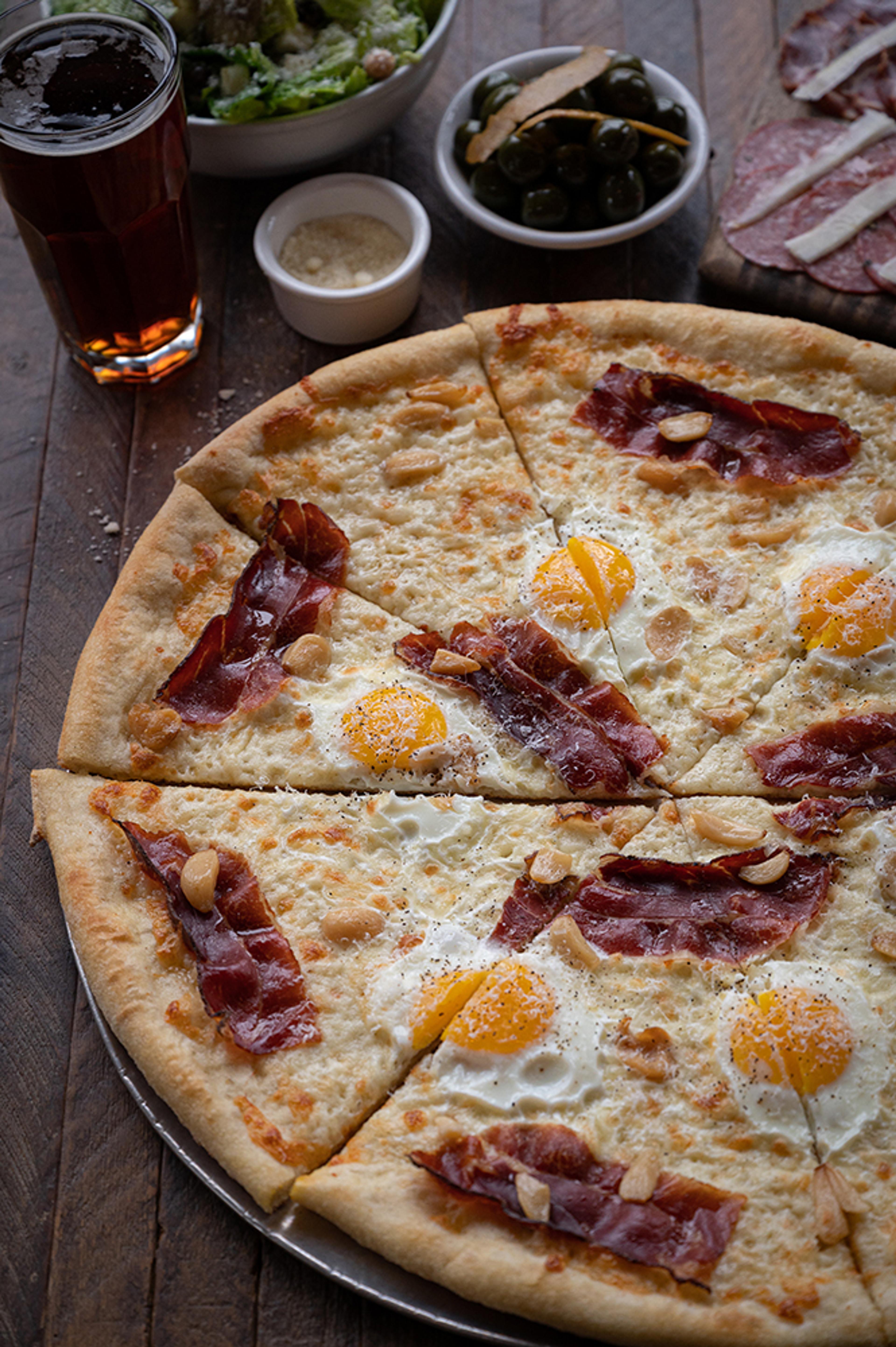Carbonara pizza topped with eggs, crispy guanciale, and garlic