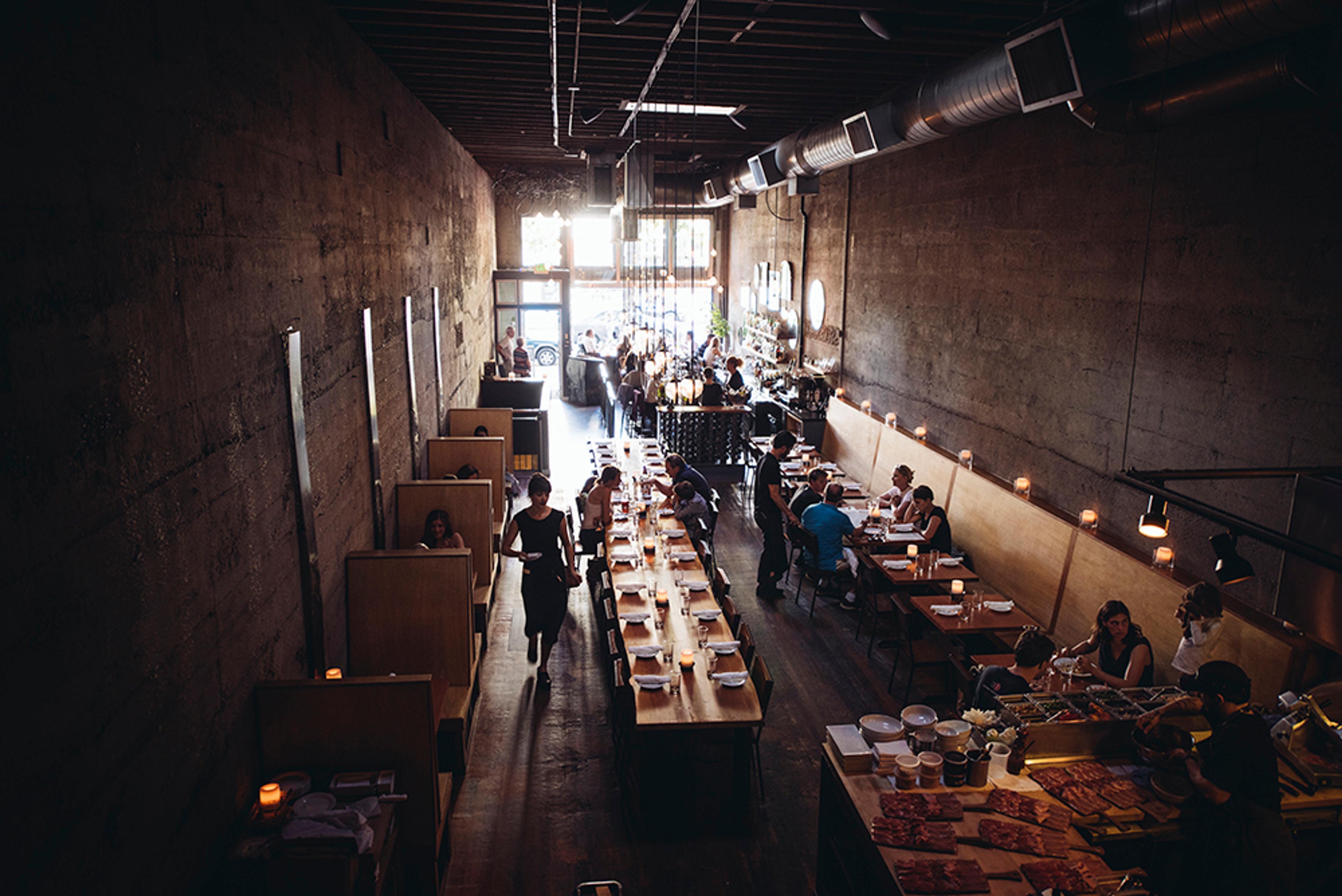 Long dimly-lit dining room with industrial elements and large communal table