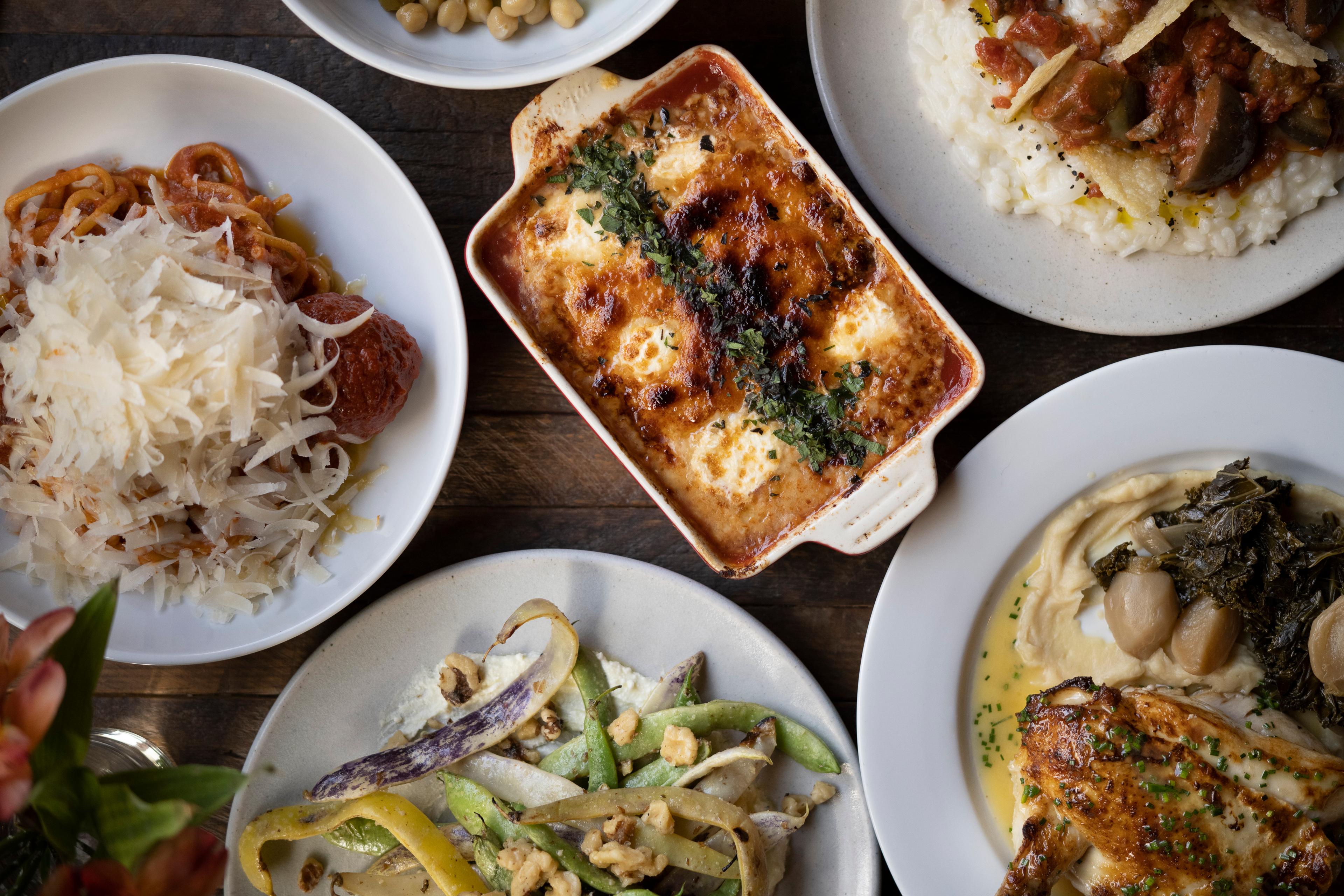 table spread with baked gnocchi, spaghetti with meatballs, chicken and mixed beans