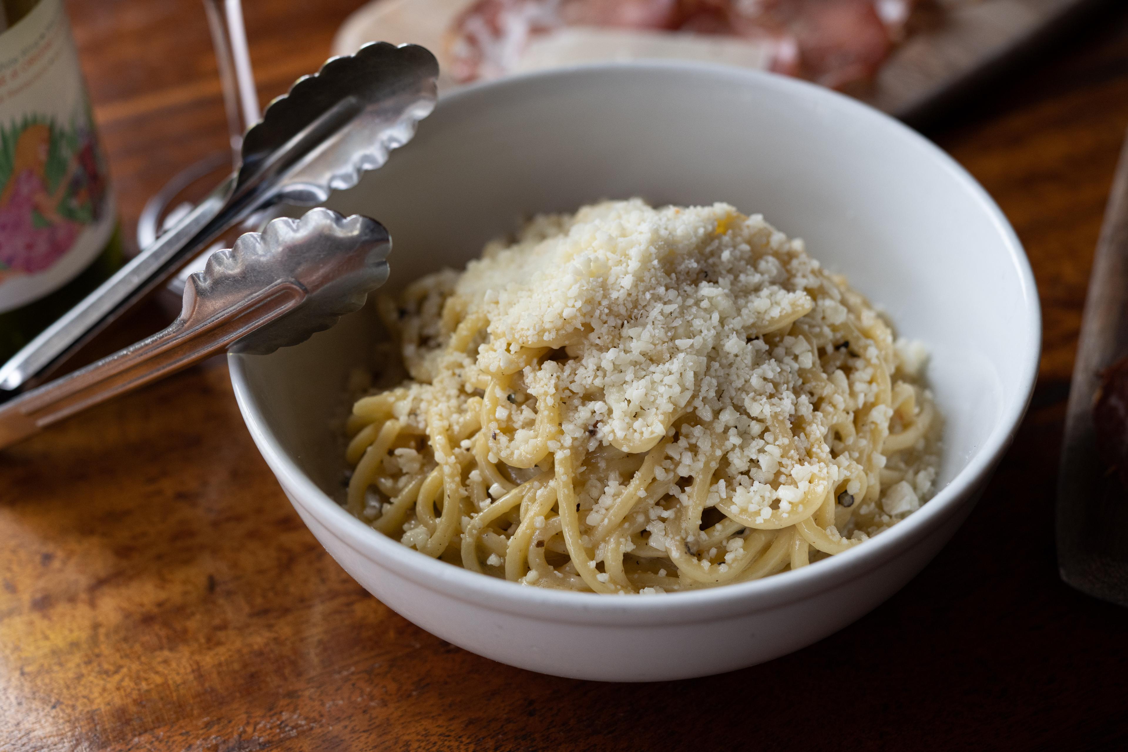 bowl of tonnarelli cacio e pepe topped with grated cheese 