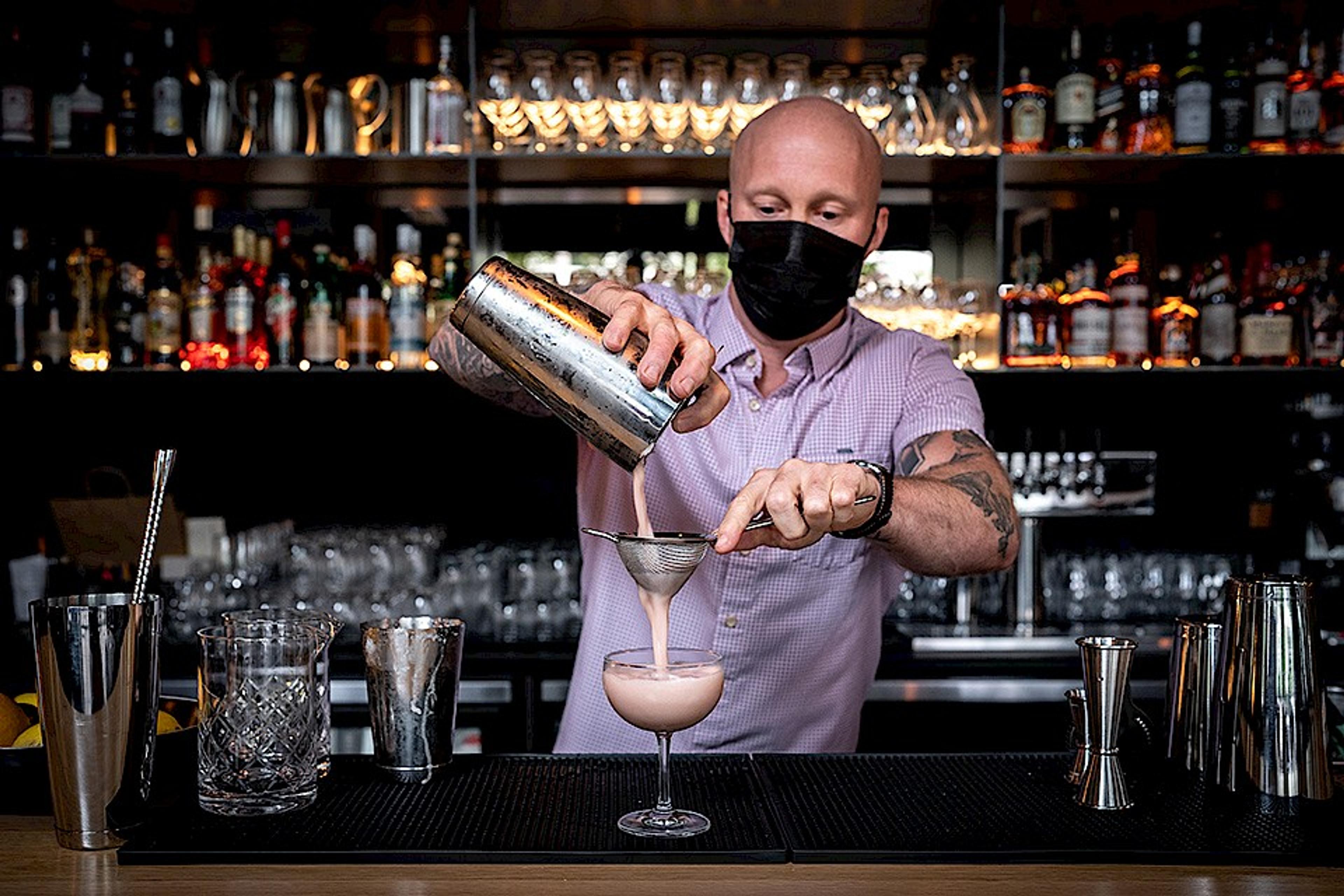 bartender straining a creamy cocktail into a coupe glass