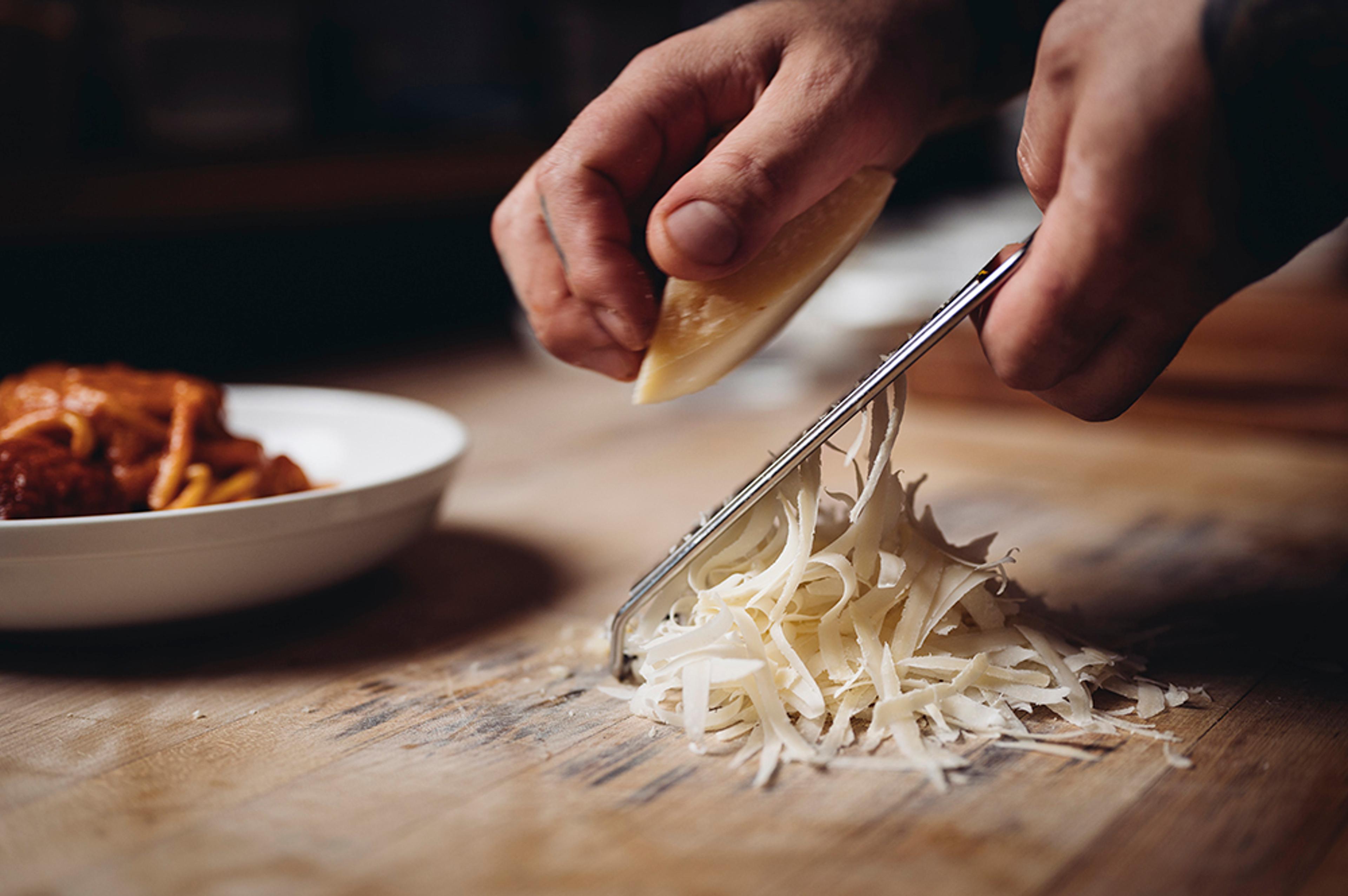 Chef hand shaving parmigiano reggiano next to bowl of pasta