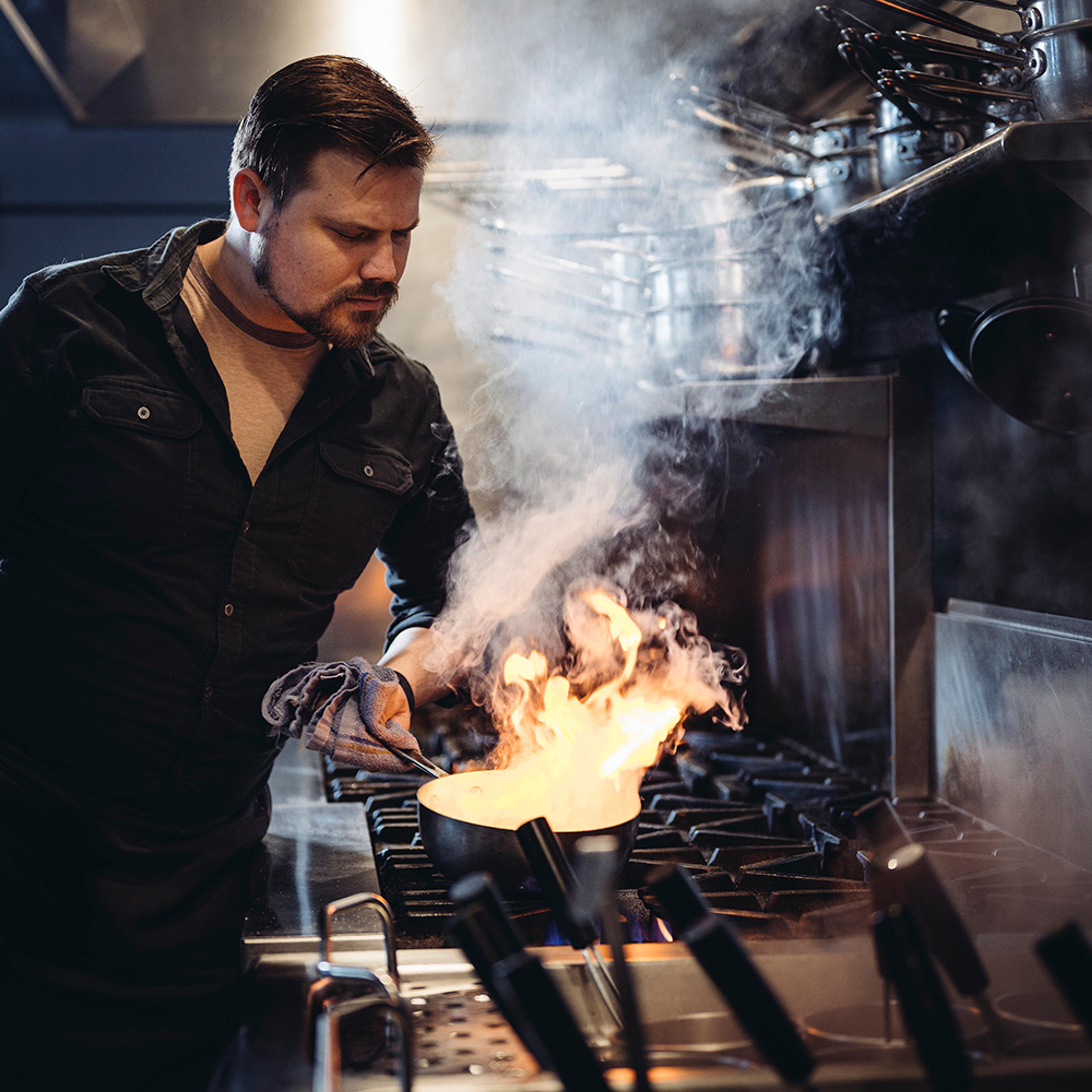 Chef cooking with flaming pan in kitchen