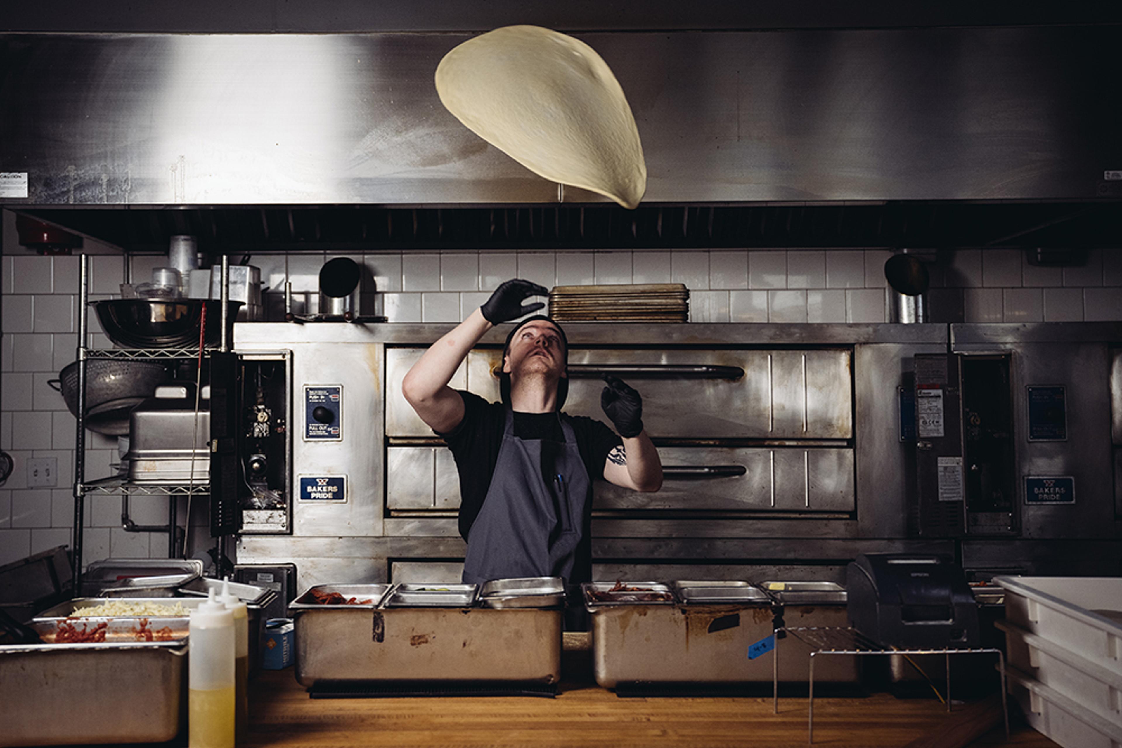 chef tossing pizza dough in kitchen