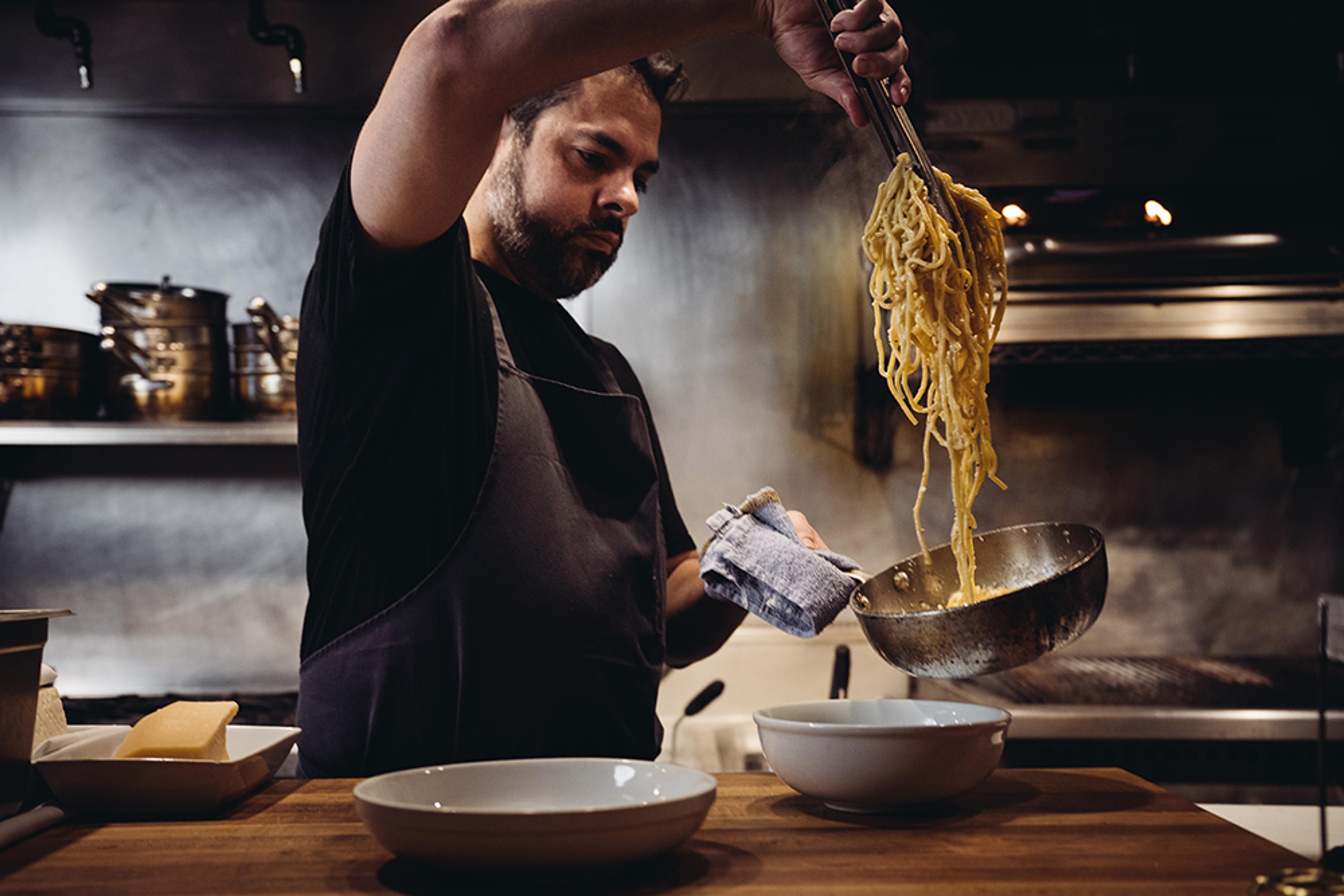 Chef pulling long cooked pasta noodles out of pot