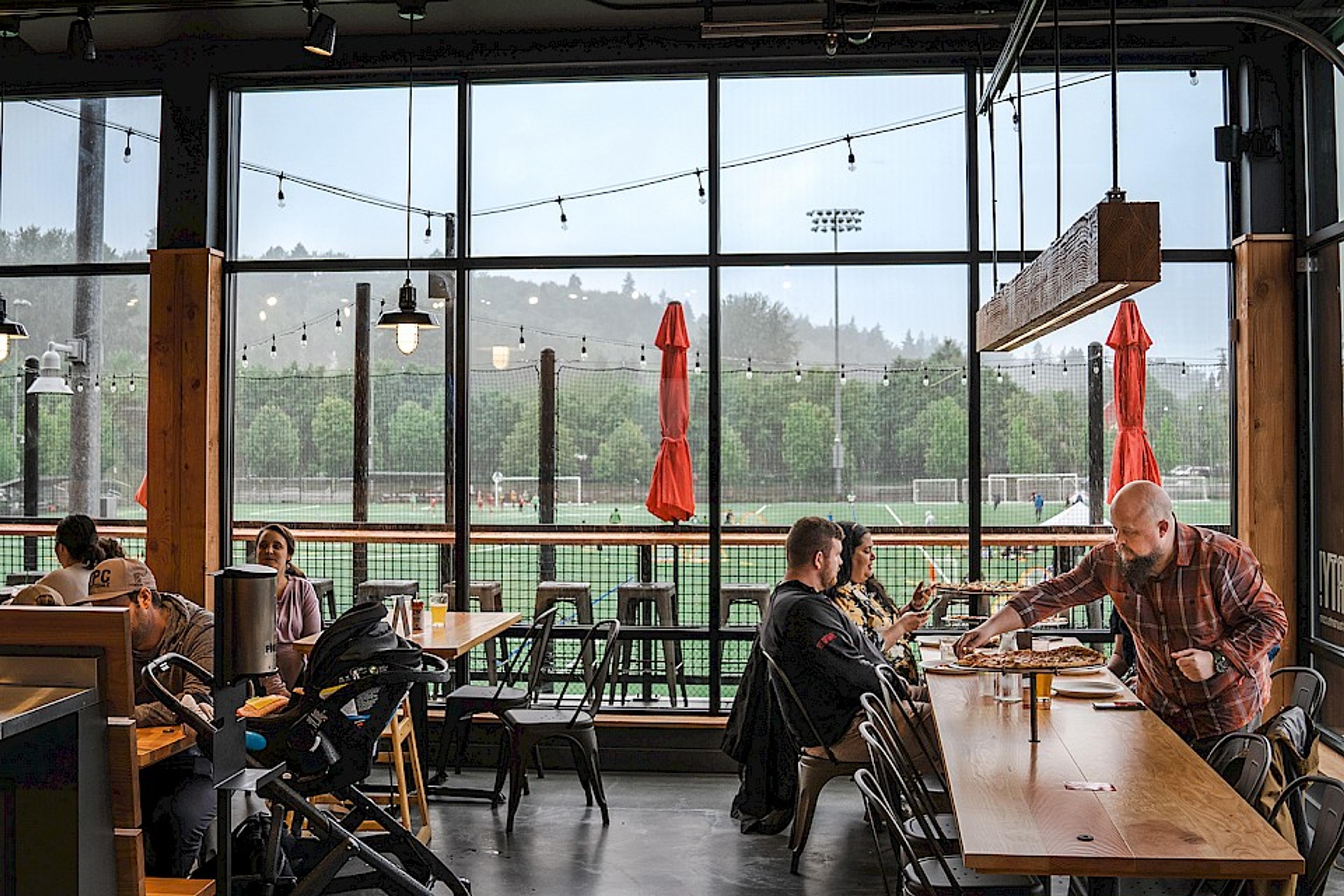 dining room with people sharing pizzas, overlooking sports fields