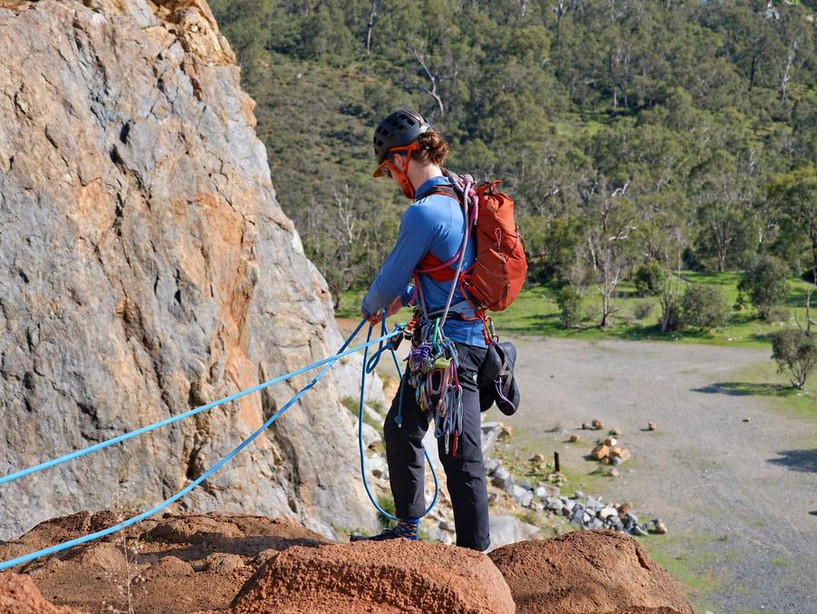 Evan at the top of a crag sorting the ropes, with bush and a dirt track far below.