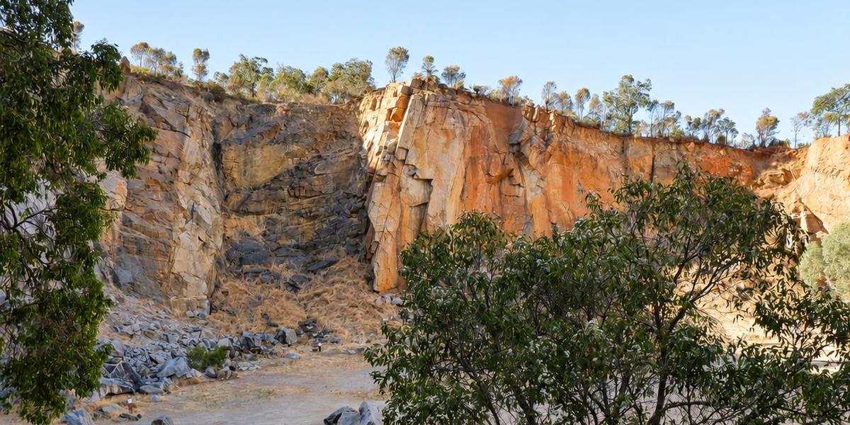A tall orange and grey quarry wall in late afternoon light, framed by gum trees.