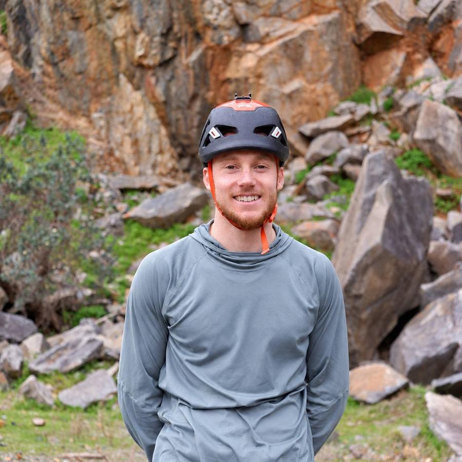 Evan smiling in his climbing helmet in front of a rocky crag.