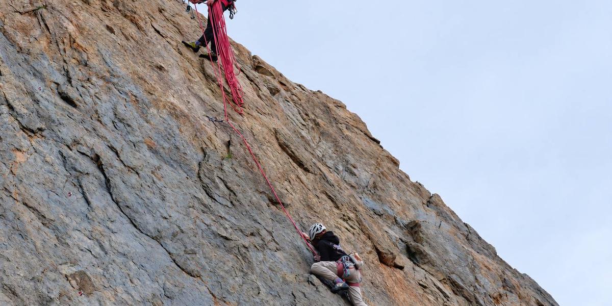 Evan belaying from the top of a crag as a climber works up the rock face below.