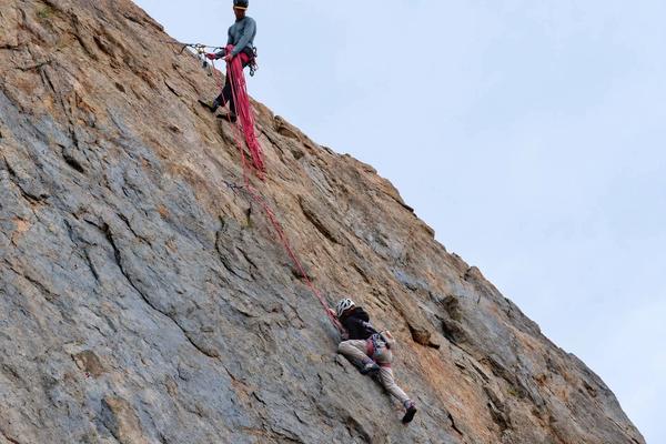 Evan belaying from the top of a crag as a climber works up the rock face below.