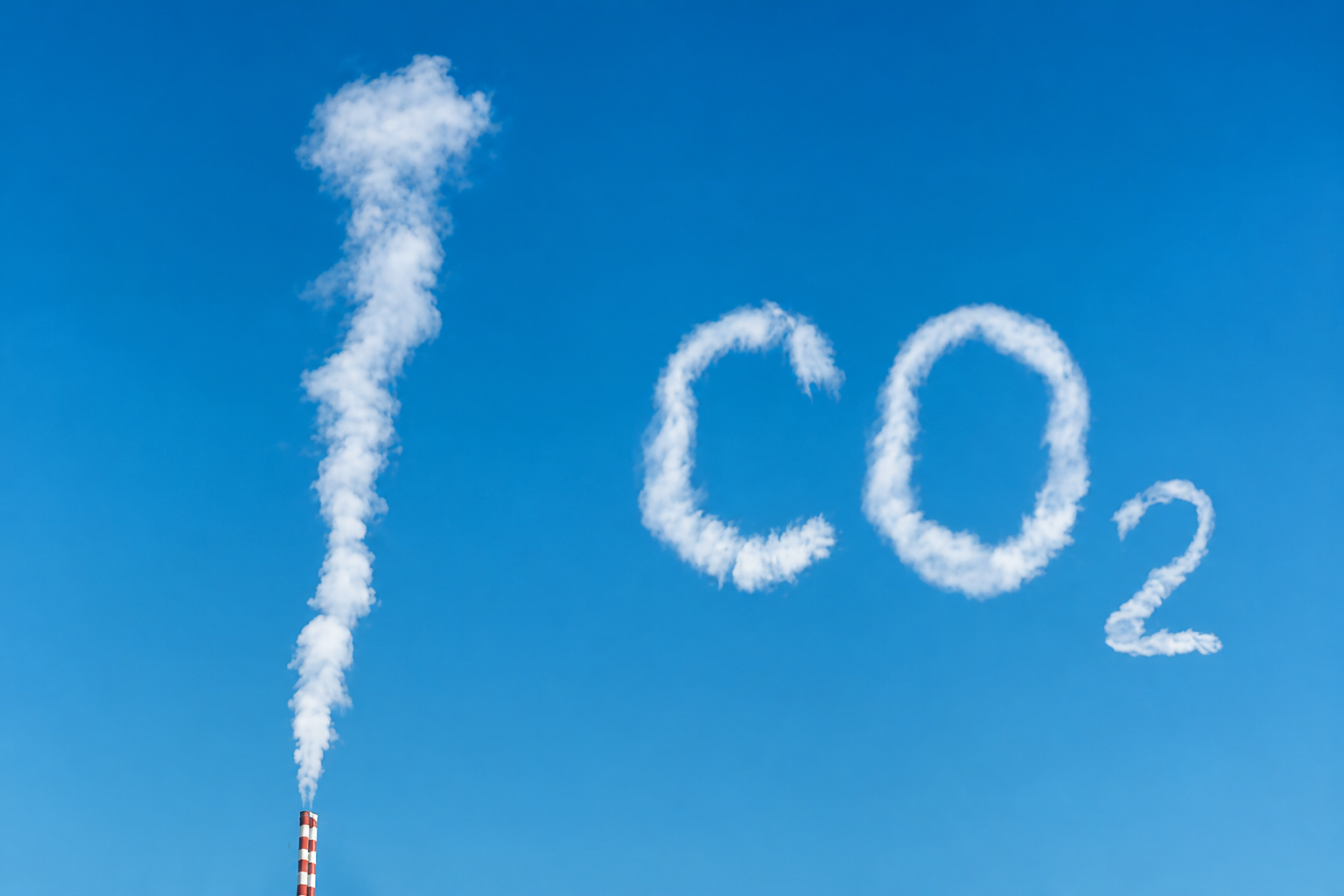 Il fumo bianco di una ciminiera forma «100 CO₂» nel cielo azzurro