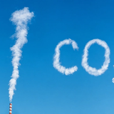 Il fumo bianco di una ciminiera forma «100 CO₂» nel cielo azzurro