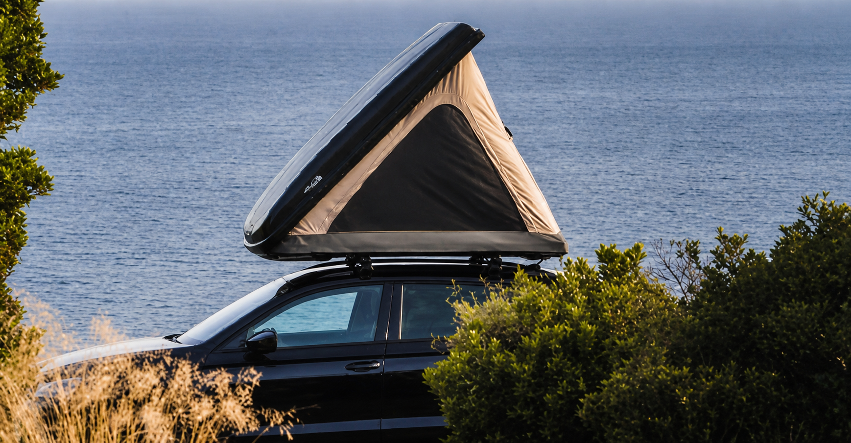 Una tenda da tetto rigida aperta a cuneo su un’auto nera affacciata sul mare
