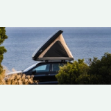 An open wedge-shaped hard-shell rooftop tent on a black car overlooking the sea