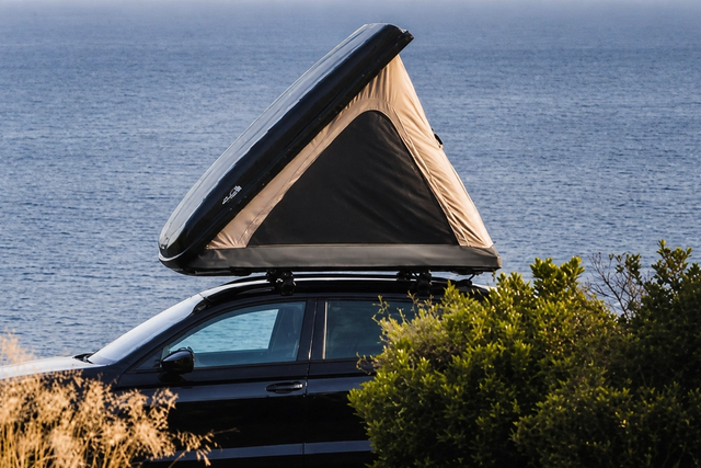 An open wedge-shaped hard-shell rooftop tent on a black car overlooking the sea