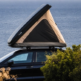 Una tenda da tetto rigida aperta a cuneo su un’auto nera affacciata sul mare