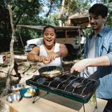 Due campeggiatori cucinano accanto a un veicolo in un campeggio nel bosco