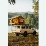 Yellow soft-shell rooftop tent opened beside a lake