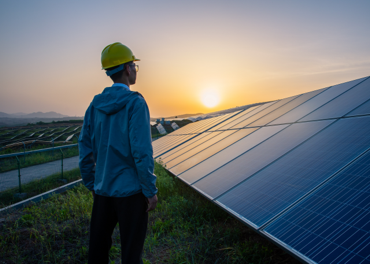 Man in a hard hat standing in a solar field with panels in the background