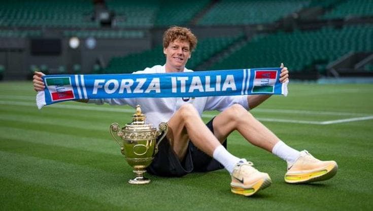 Sinner seduto sull’erba del Centre Court con trofeo e sciarpa “Forza Italia”.