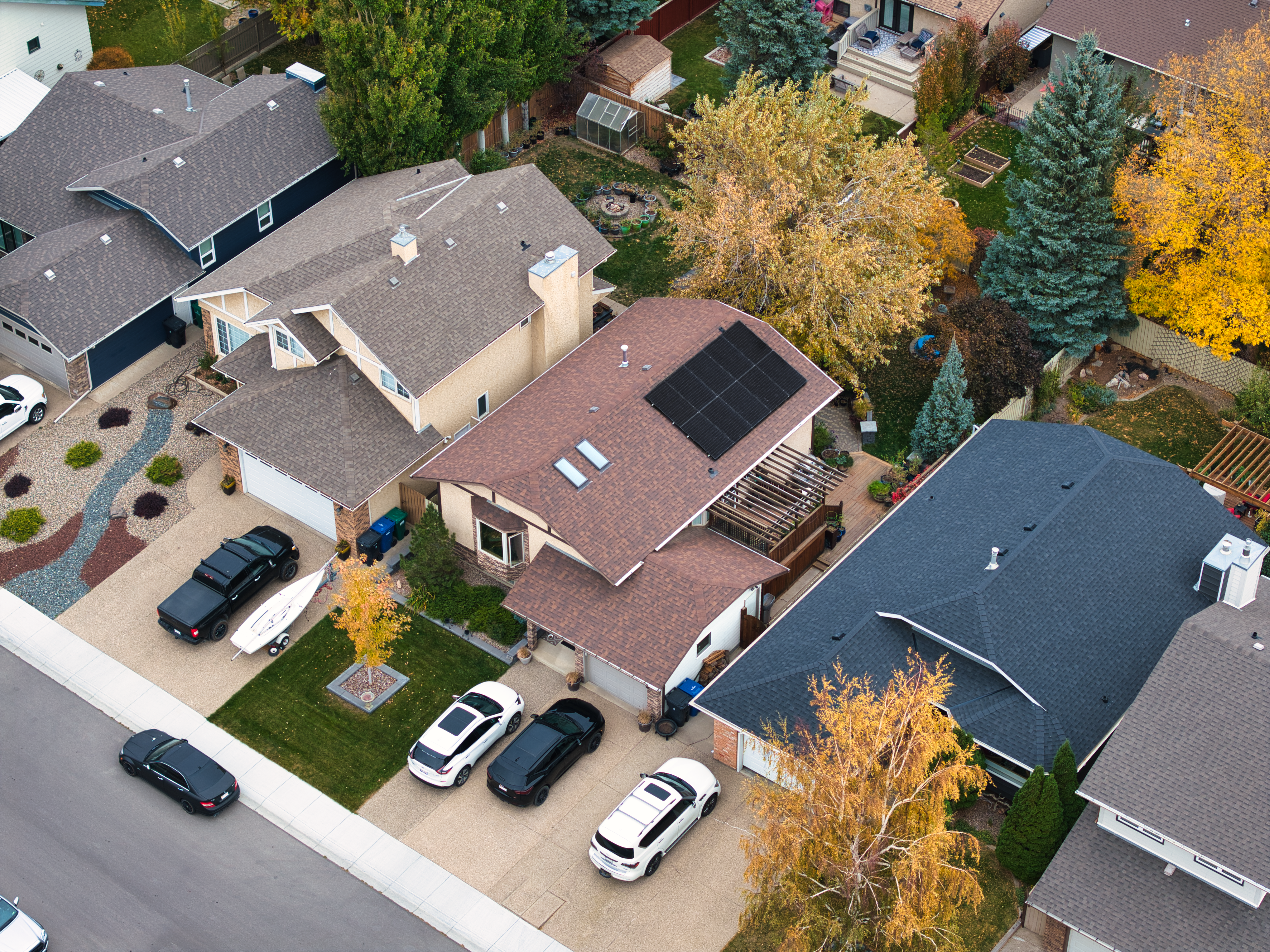 High-angle aerial drone photograph of a clean residential solar panel installation by Firefly Solar, showing an all-black module array positioned on a brown asphalt shingle roof in an Alberta suburban neighborhood.