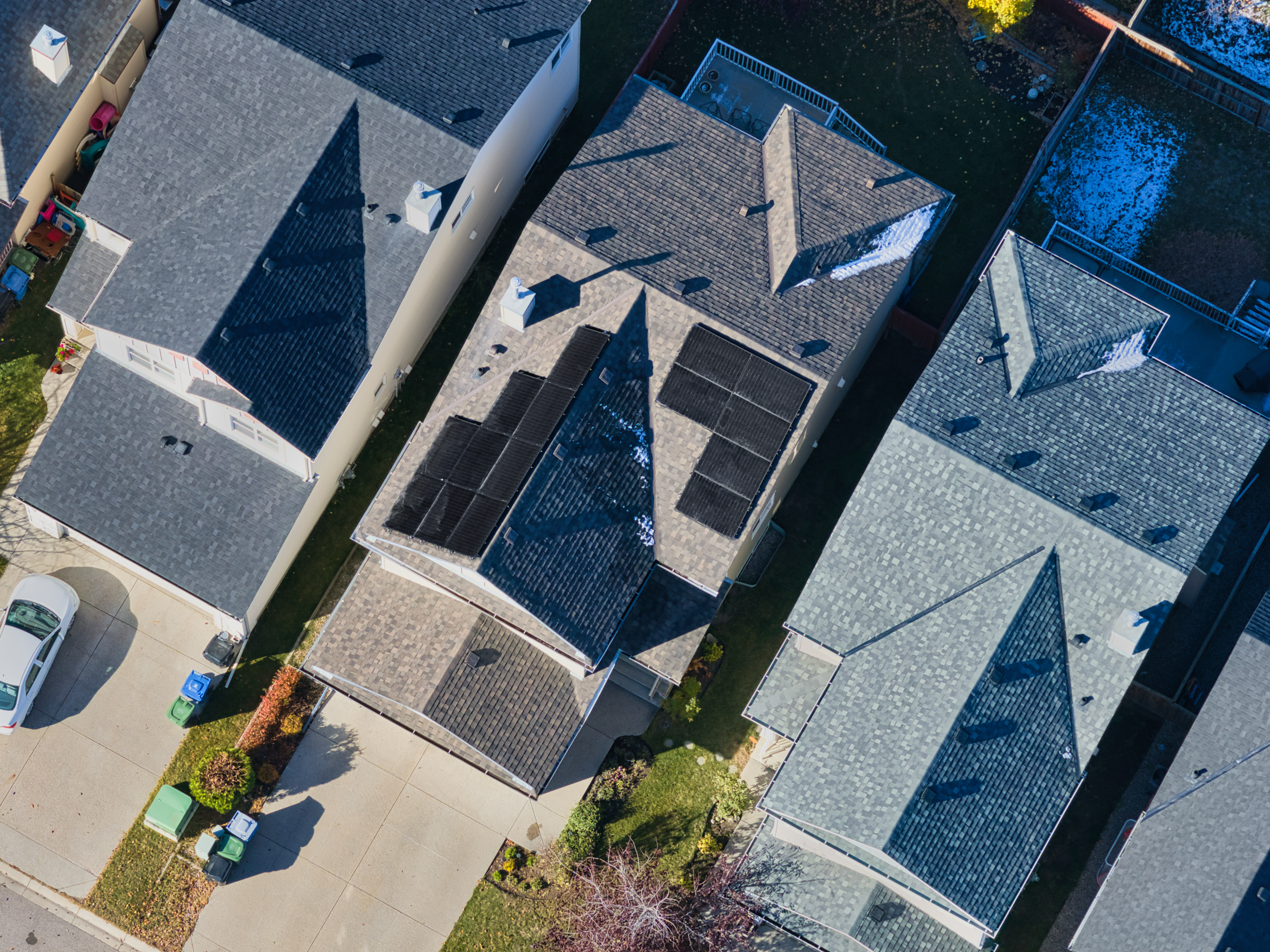 Aerial drone view of a professional residential solar panel installation by Firefly Solar on a multi-gabled roof in an Alberta suburban neighborhood, showcasing a custom residential solar array engineered to fit complex roof angles.