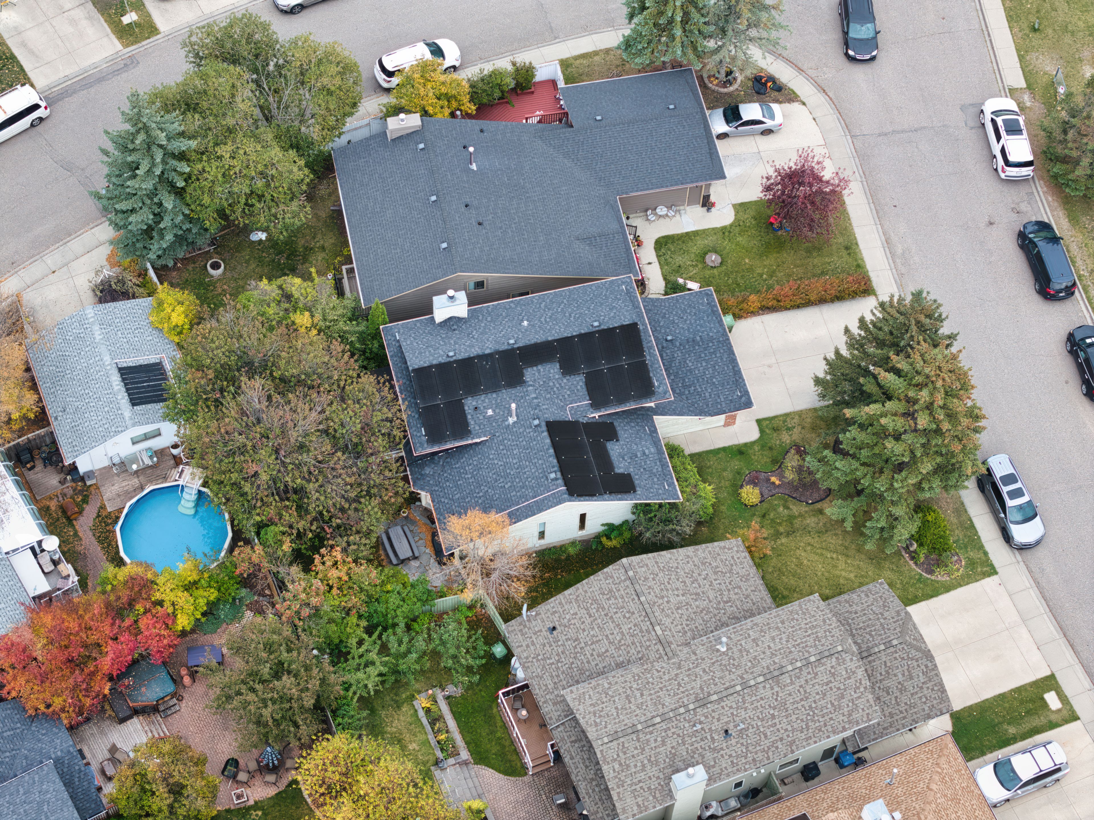 Aerial drone view of a home solar installation by Firefly Solar on a dark shingled roof, featuring sleek black panels in a multi-array layout on an Alberta property next to a backyard pool.