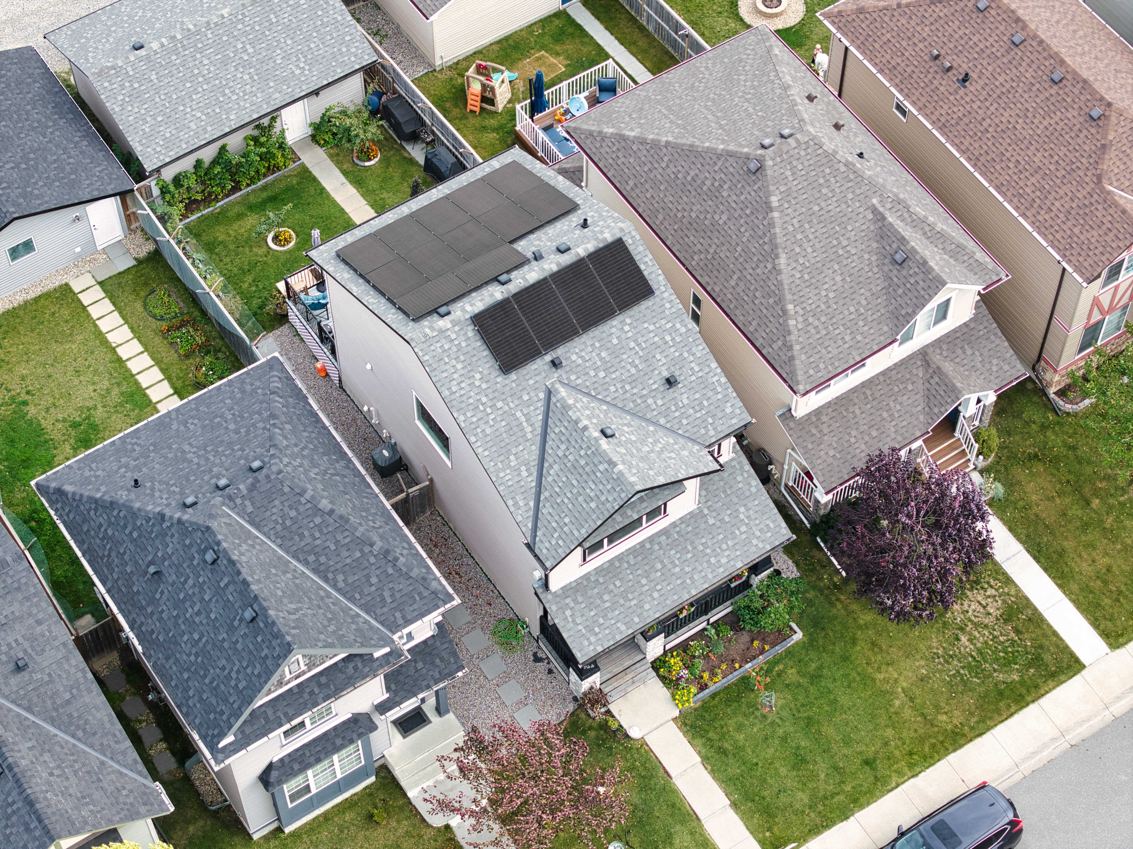 High-angle aerial drone photograph of a modern residential solar panel installation by Firefly Solar on a light gray shingled roof, showcasing a neat split-array configuration on a two-story home in an Alberta neighborhood.