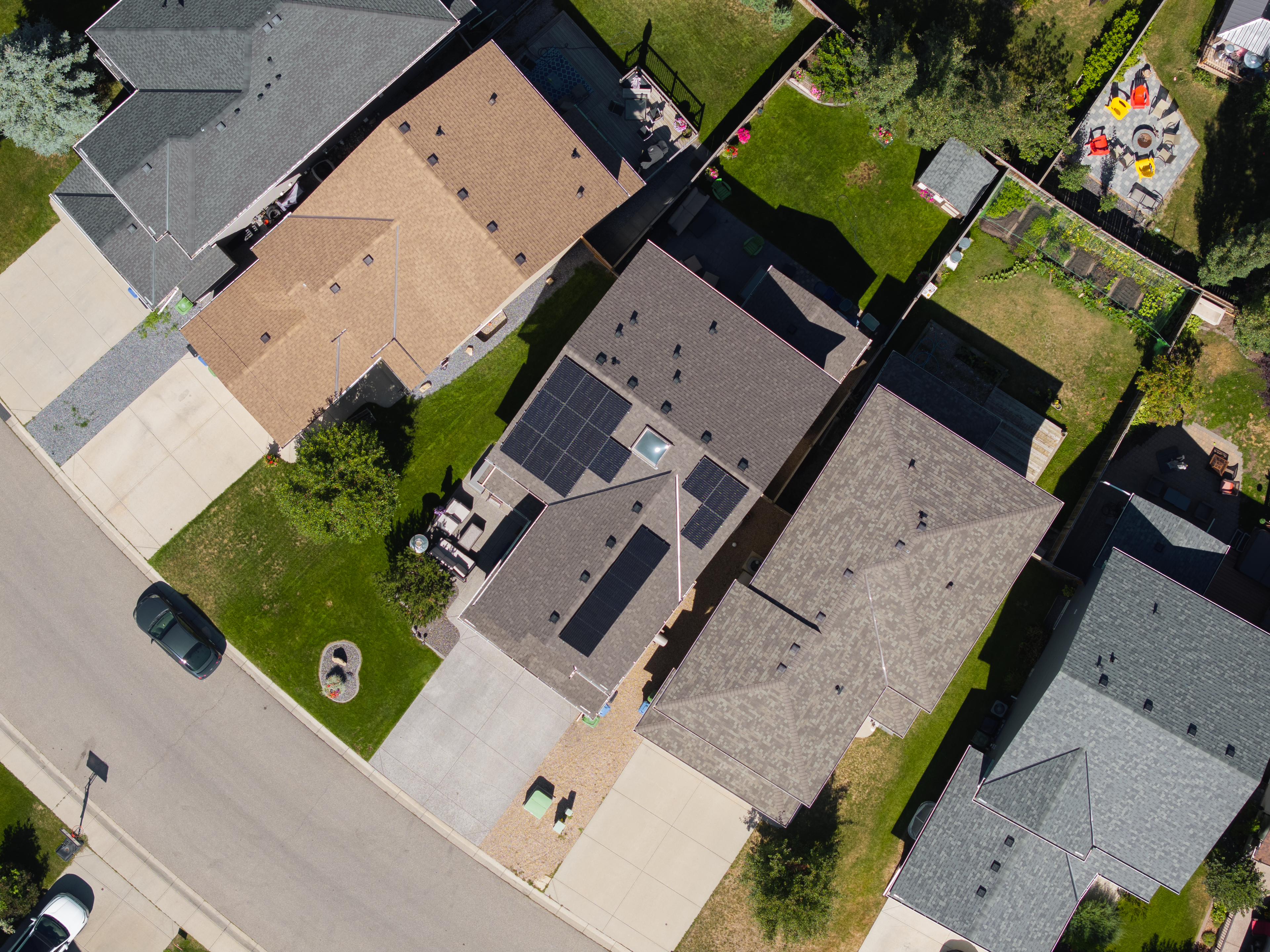 Top-down aerial drone view of a premium residential solar panel installation by Firefly Solar on a dark grey shingled roof, featuring sleek all-black solar modules distributed across multiple roof faces of a suburban Alberta home.