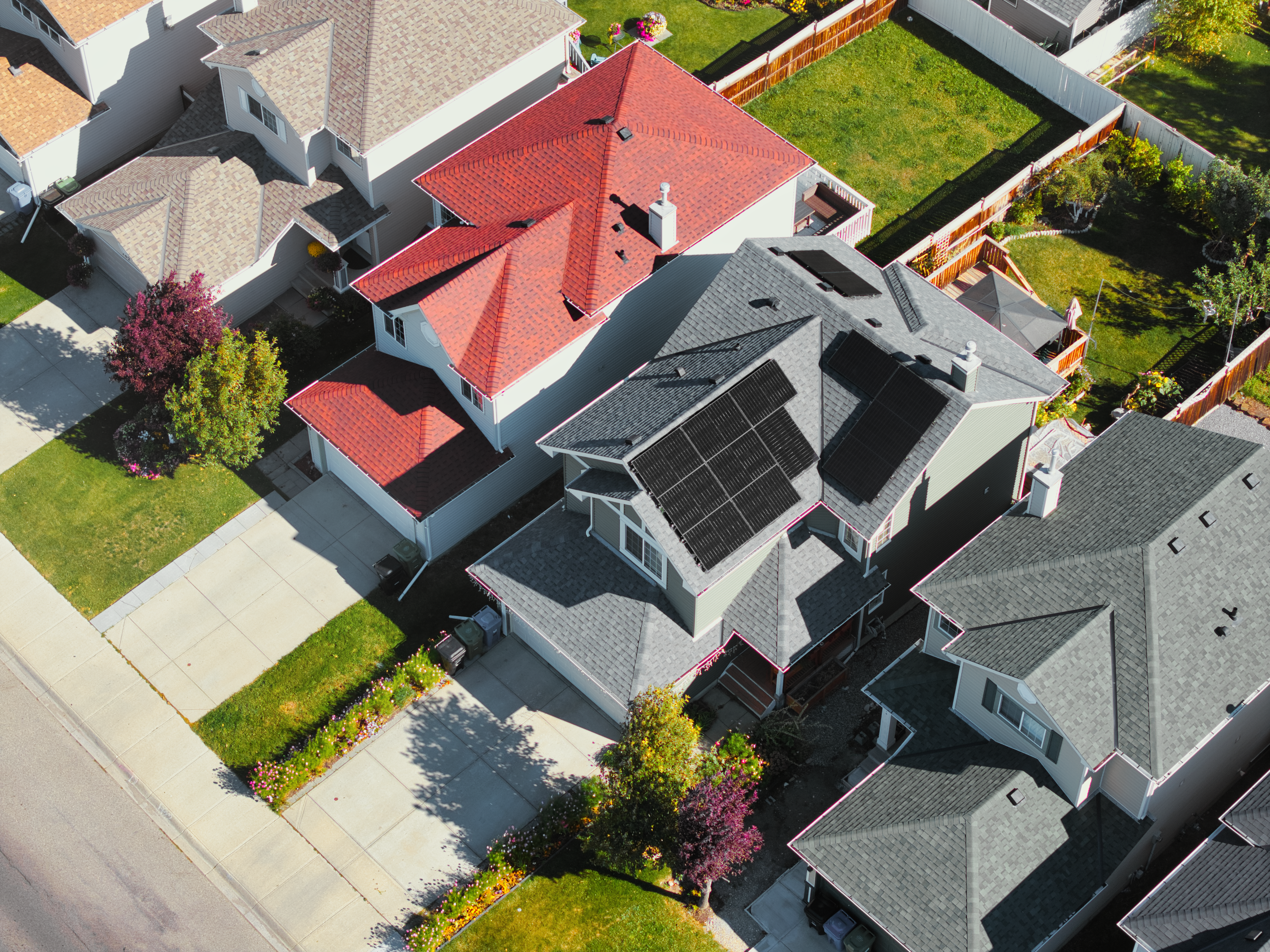 High-angle aerial drone view of a clean home solar installation by Firefly Solar on a multi-tiered grey asphalt shingle roof, displaying high-efficiency black solar panels optimized for maximum sunshine exposure on an Alberta residence.
