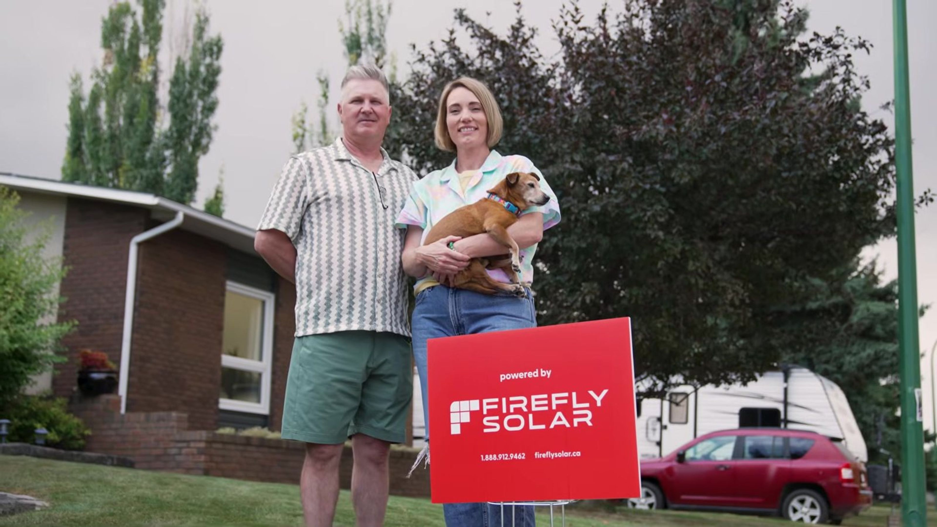 Todd and Stacey holding their dog beside a Firefly Solar yard sign outside their Lethbridge home