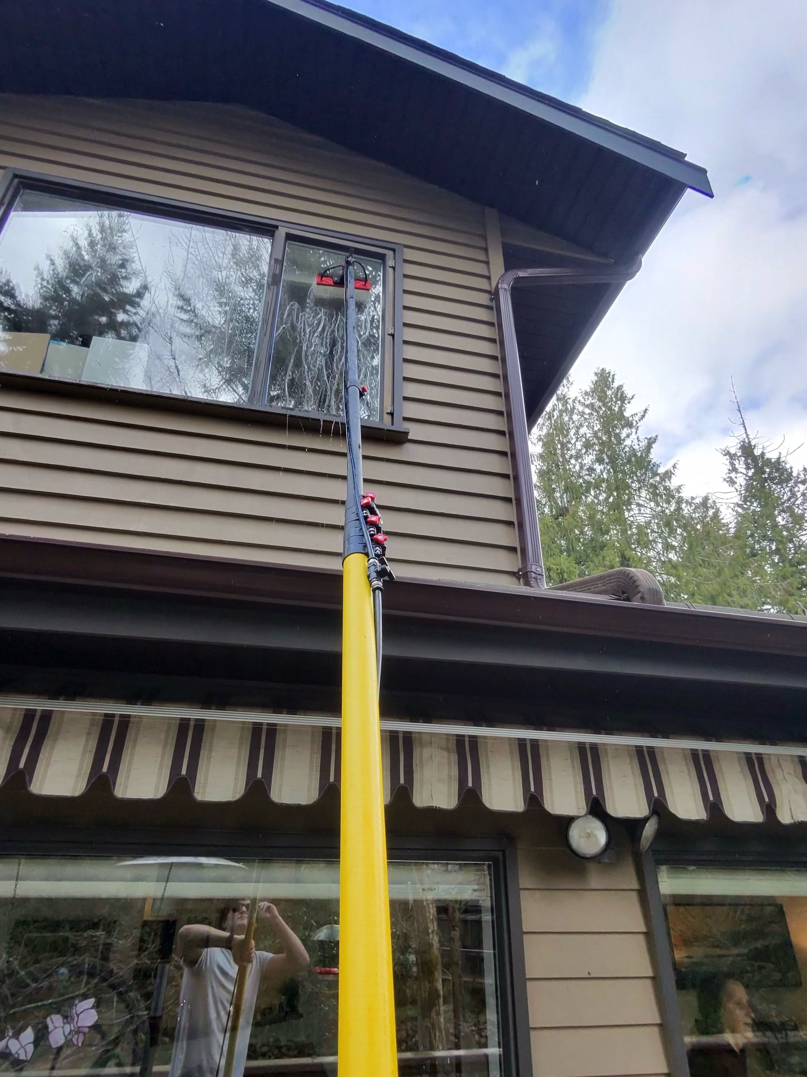 Winning Window Cleaning technician extending a water-fed pole to reach upper-storey windows on a two-storey Victoria BC home