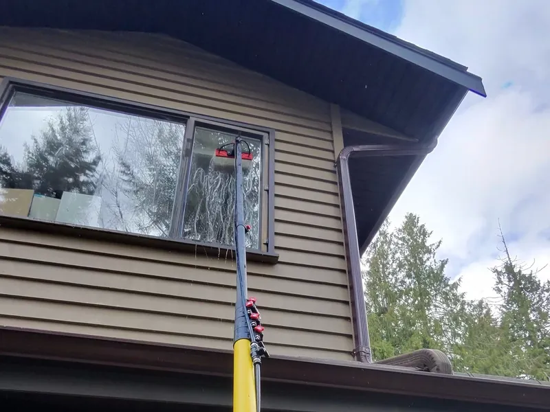 Winning Window Cleaning technician extending a water-fed pole to reach upper-storey windows on a two-storey Victoria BC home