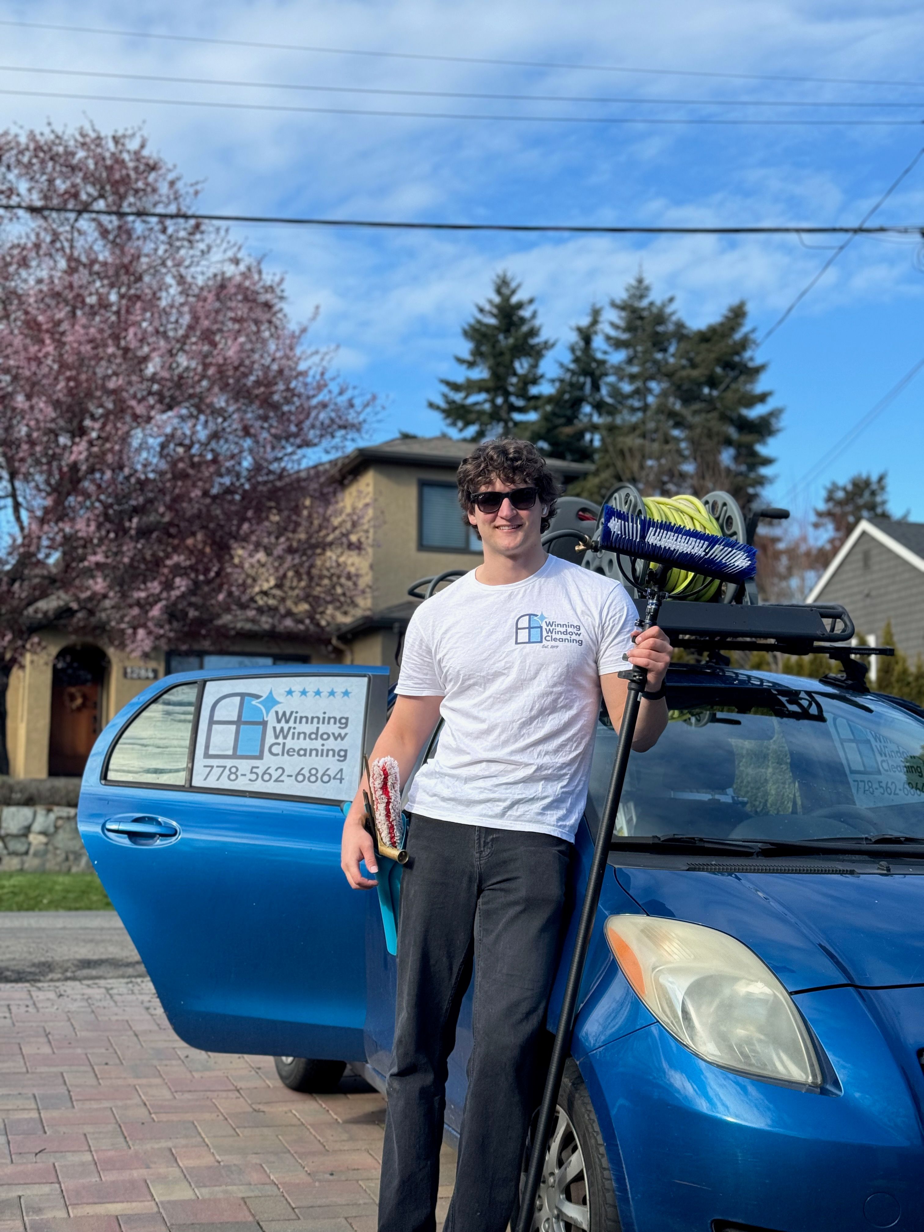 Sean, owner of Winning Window Cleaning, holding a water-fed pole beside his branded vehicle in Victoria BC