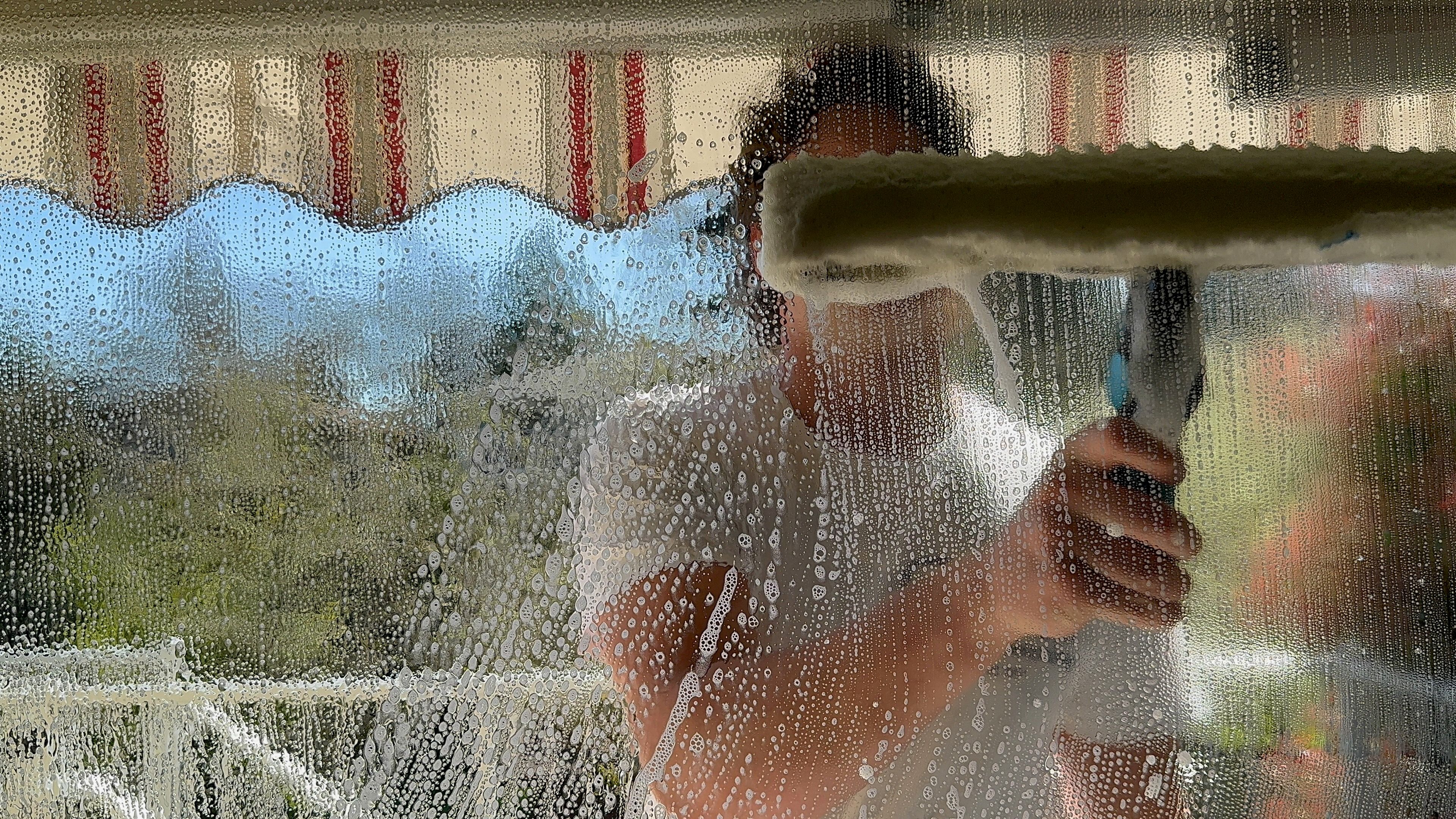 View through a wet soapy window pane as a Winning Window Cleaning technician scrubs the exterior glass with a washer sleeve in Victoria BC
