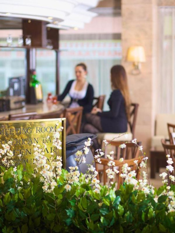 Interior de bar elegant, cu două femei la masă, flori albe și un semn cu denumirea încăperii.