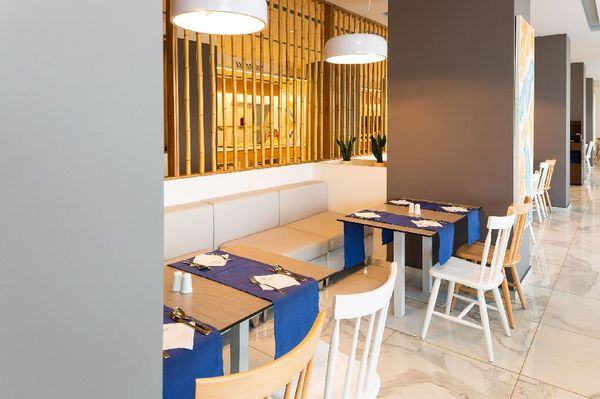 Interiorul unui restaurant modern, cu mese decorate în albastru, scaune albe și un decor elegant din lemn.