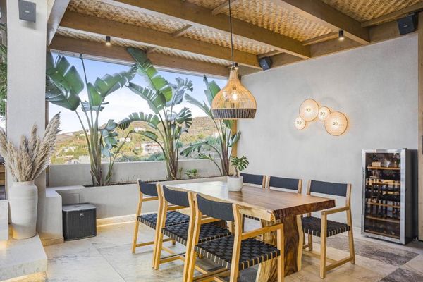 Terasă modernă, cu masă din lemn și scaune, plante verzi și iluminat decorativ. Vedere panoramică pe fundal.