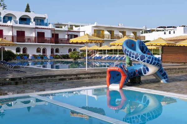 Piscină cu tobogan colorat, șezlonguri, umbrele galbene și clădiri albe în fundal. Atmosferă de vacanță relaxantă.