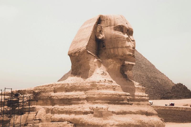 Marele Sfinx din Giza, Egipt, cu piramida în fundal, sub un cer luminos deșertic.