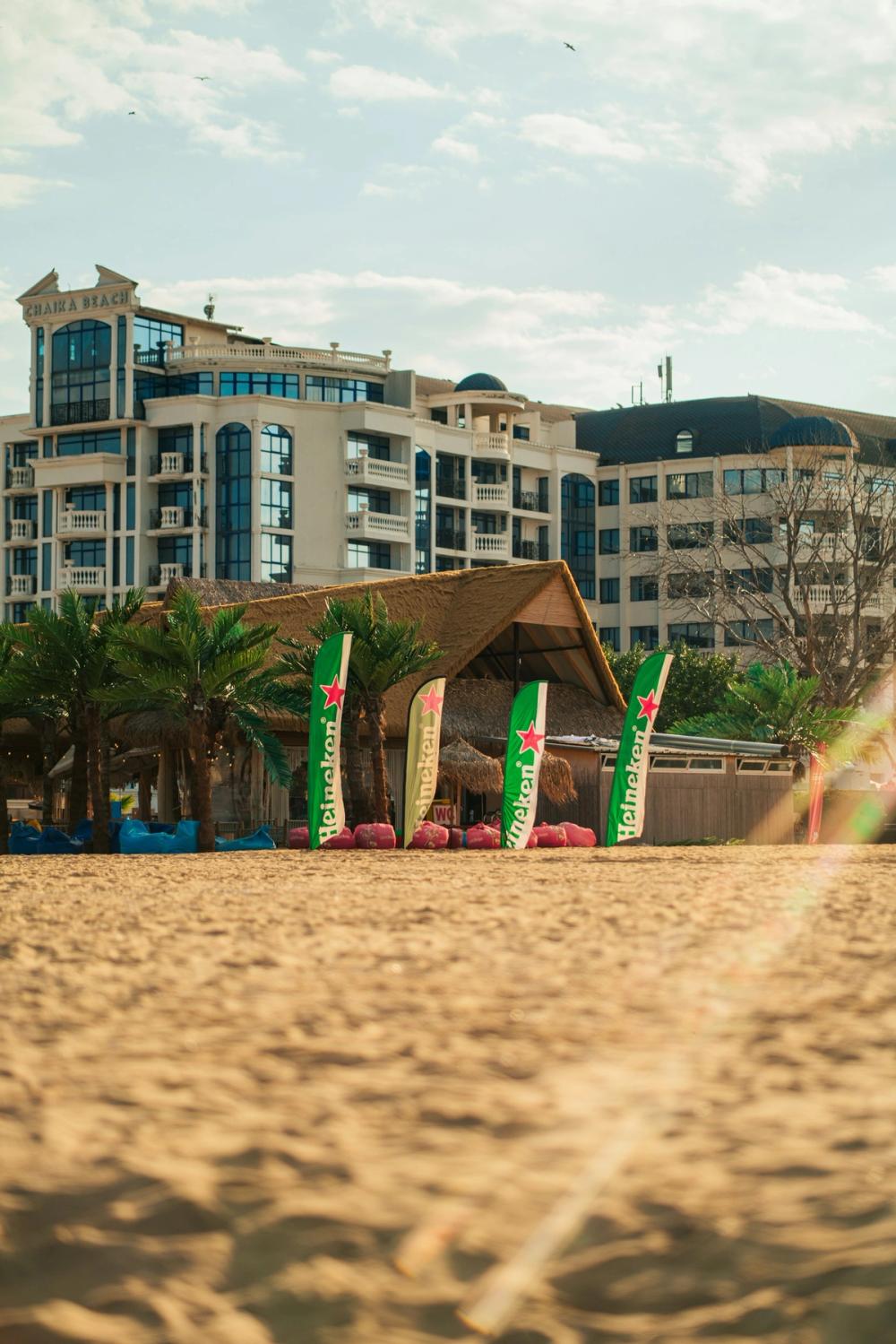 Plaja Sunny Beach din Bulgaria cu nisip, palmieri artificiali și hoteluri în fundal.