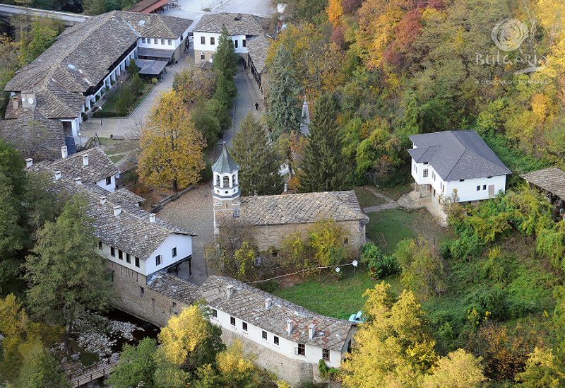 Schitul Sf. Arhanghel Mihail din Bulgaria, văzut de sus, înconjurat de pădure și clădiri tradiționale.
