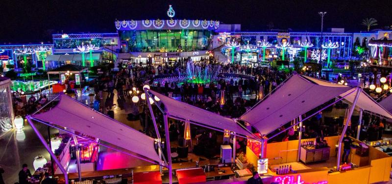 Soho Square din Sharm El Sheikh iluminat noaptea, cu fântână colorată și mulțime animată.