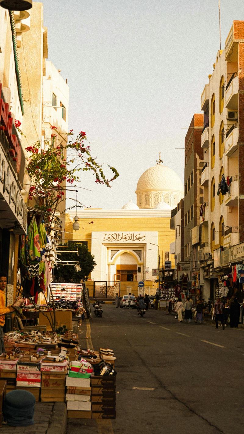Stradă animată în Hurghada, Egipt, cu magazine locale și o moschee cu cupolă albă în fundal.