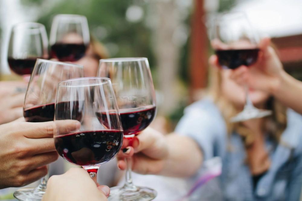 Oameni ciocnind pahare cu vin roșu într-un moment de socializare și sărbătoare.