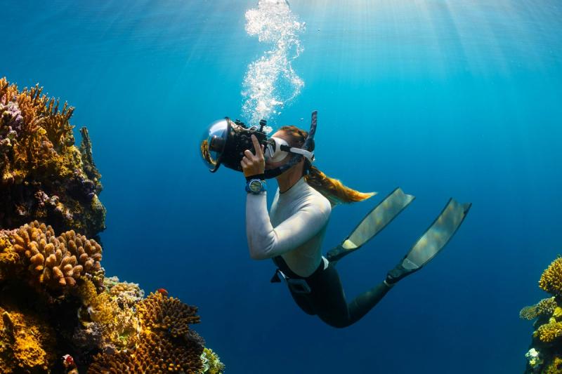 Scafandru care explorează recifuri de corali colorate, fotografiind viața subacvatică într-o zonă tropicală. Imagine subacvatică spectaculoasă ce ilustrează frumusețea oceanului și pasiunea pentru explorare marină.