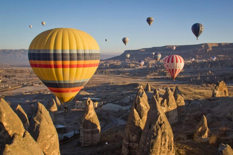 Baloane cu aer cald colorate plutind deasupra peisajului stâncos și a formațiunilor unice de piatră din Cappadocia la răsărit.